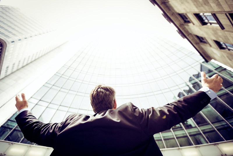 man in suit with arms wide looking up amont tall buildings